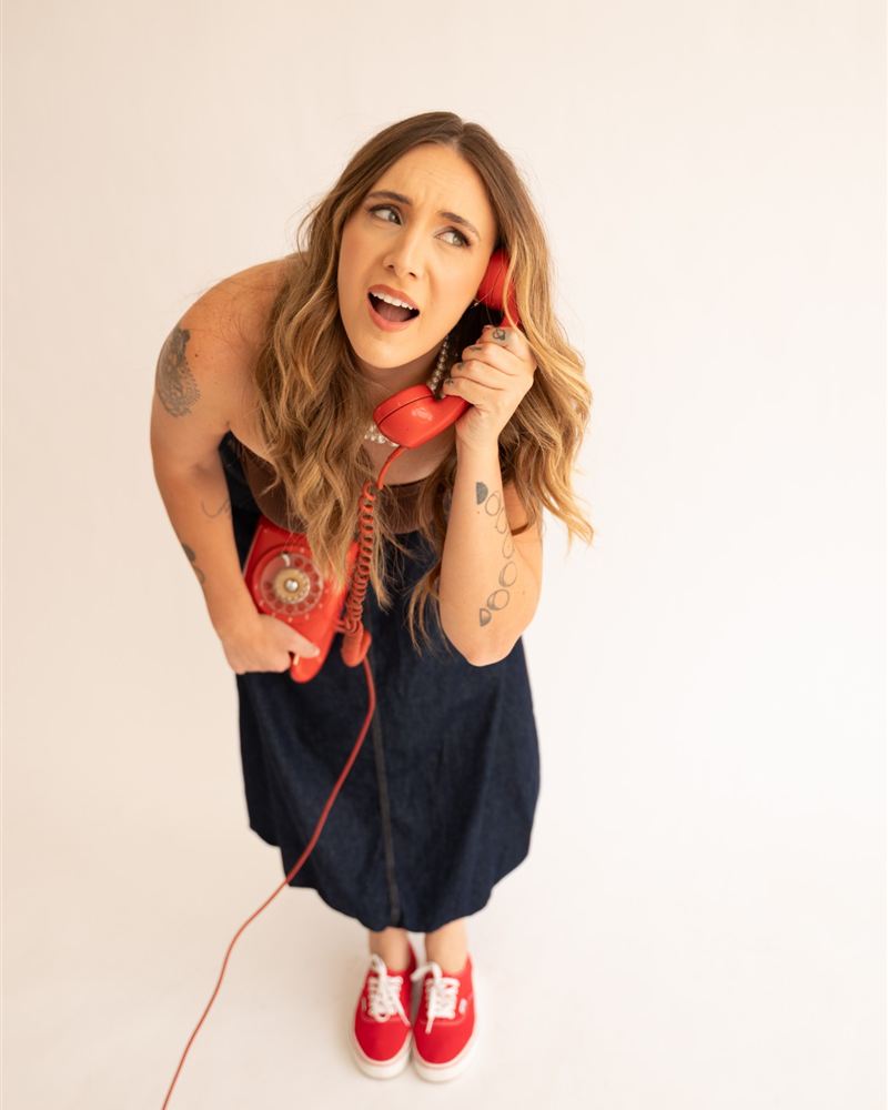 Amanda Drebes de vestido jeans e tênis vermelho, falando em um telefone vermelho antigo